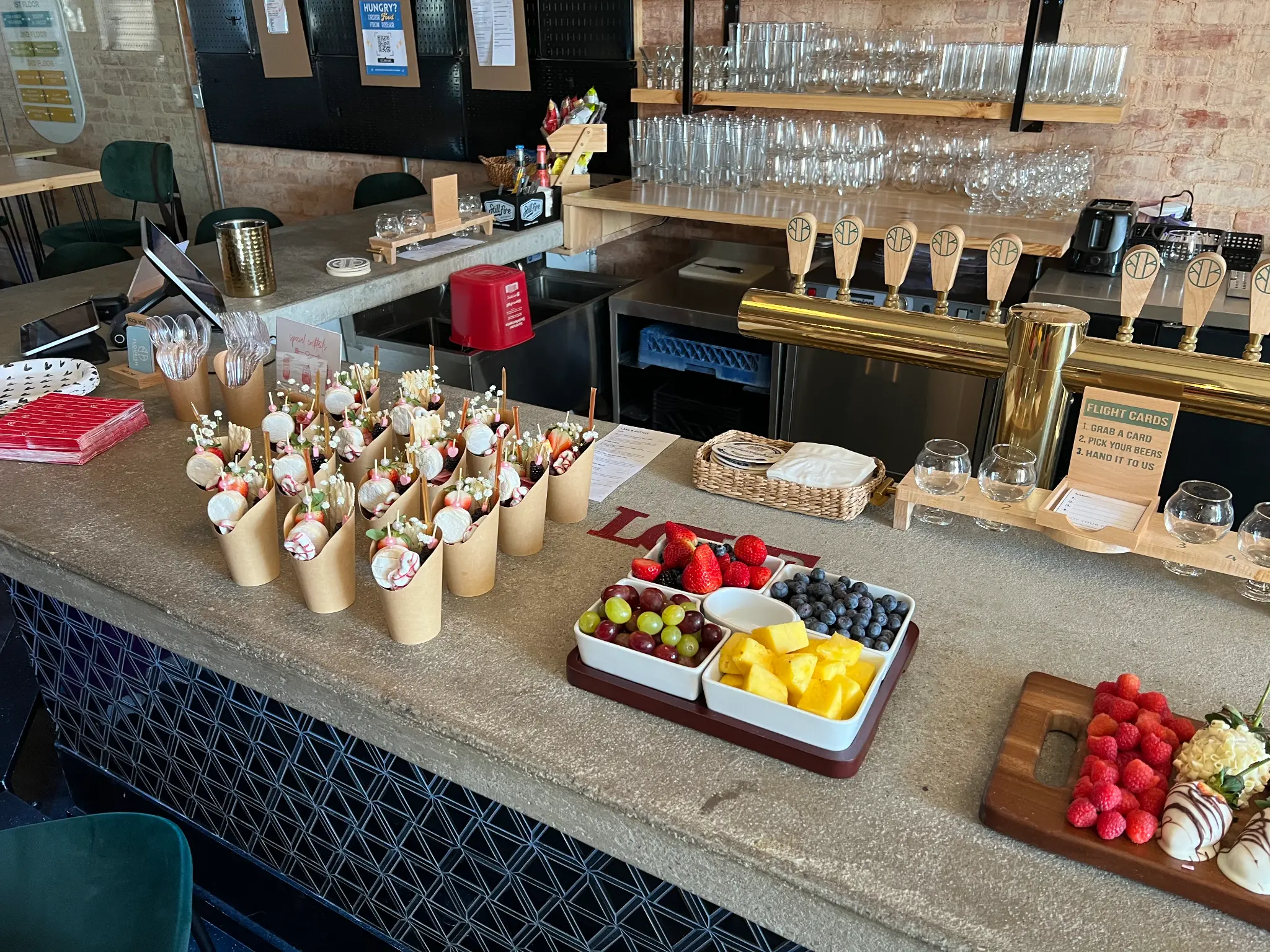 Flourish Taproom bar set up for a private event with charcuterie cones, fresh fruit, and chocolate strawberries on the concrete bar top