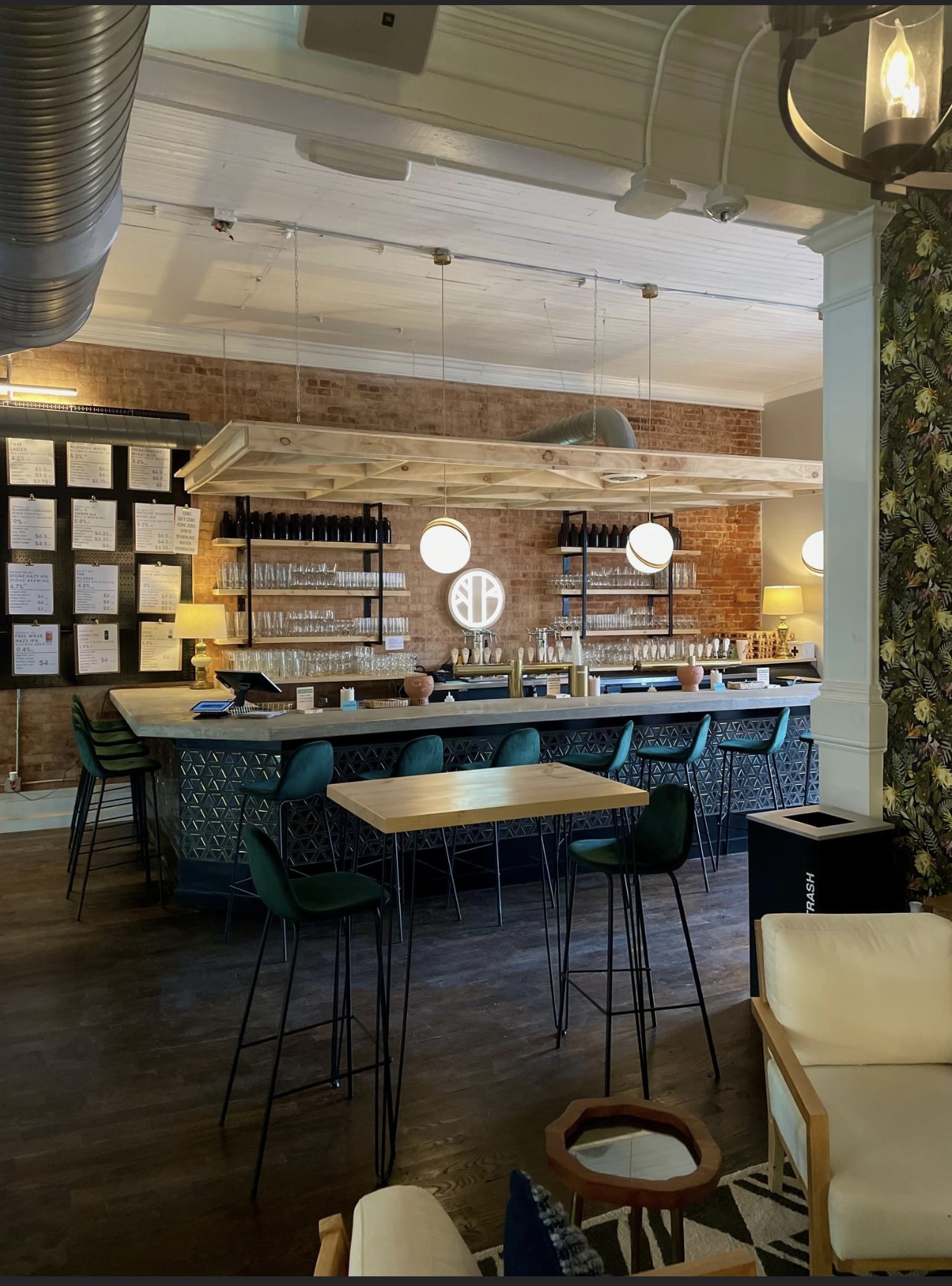 Flourish Taproom interior — exposed brick bar with teal stools, warm globe lights, and the Flourish logo illuminated on the wall